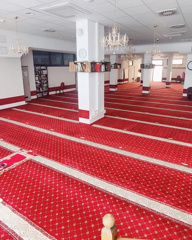 Der Gebetsraum der Moschee: roter Gebetsteppich mit hellen Bordüren, Kristallleuchter und Bücherregale